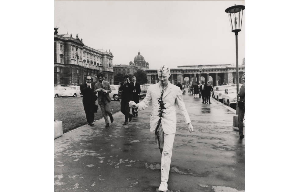 Günter Brus, Wiener Spaziergang [Βόλτα στην Βιέννη], 5 Ιουλίου 1965, Βιέννη, Φωτογραφία: [[#Ludwig Hoffenreich#]]. Κατά την δράση αυτή, ο Brus θα επιχειρήσει να περπατήσει στο κέντρο της Βιέννης καλυμμένος σε όλο του το σώμα με λευκή μπογιά. Μια μαύρη γραμμή σαν ουλή, διαγράφεται από την κορυφή του κεφαλιού του έως τα δάχτυλα του δεξιού του ποδιού, χωρίζοντας το σώμα του στα δύο. Ο Brus κατάφερε να κάνει μόλις λίγα βήματα, καθώς η αυστριακή αστυνομία διέκοψε τον περίπατό του, επιβάλλοντάς του χρηματικό πρόστιμο.