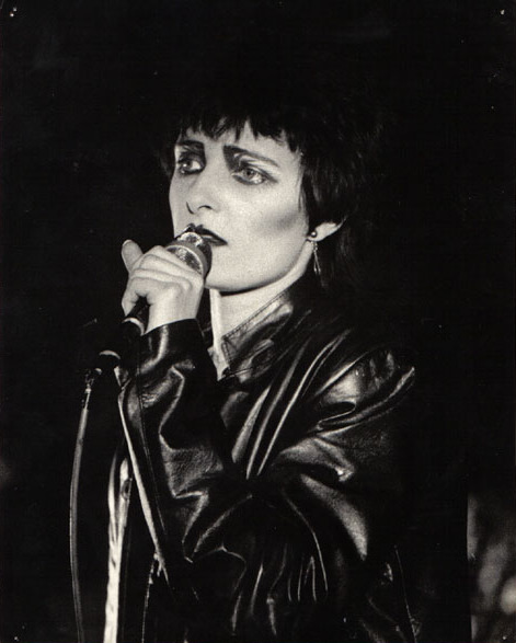 Η [[#Siouxsie Sioux [Σιούζι Σιού]#]], ηγετική μορφή του συγκροτήματος&nbsp;[[#Siouxsie and the Banshees#]], σε ζωντανή εμφάνιση στο Tiffany's του Εδιμβούργου το 1980. Η καλλιτέχνις αποτέλεσε κεντρικό πρόσωπο για τη διαμόρφωση της γοτθικής αισθητικής στη μουσική και τη μόδα, εισάγοντας ένα ιδιαίτερο οπτικό ύφος που βασίζεται στο έντονο μακιγιάζ και τη σκοτεινή ενδυμασία. Η συγκεκριμένη απεικόνιση καταγράφει τη μετάβαση από το ποστ-πανκ προς τη συγκρότηση της νεογοτθικής υποκουλτούρας, αναδεικνύοντας τη σημασία της σκηνικής παρουσίας στην ανάδειξη του ανοίκειου και του μυστηριώδους.