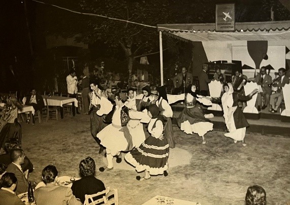 Δημοτικοί χοροί στο Α΄ μέρος επιθεώρησης πίστας σε θερινό κέντρο. Χορευτές και χορεύτριες με φουστανέλες και παραδοσιακές ενδυμασίες χορεύουν στην πίστα, ανάμεσα στα τραπέζια των θαμώνων, ενώ οι μουσικοί παίζουν σε υπερυψωμένη εξέδρα. Τα παραδοσιακά χορευτικά άνοιγαν συχνά το πρόγραμμα, ιδίως στα κέντρα της Πλάκας με τουριστικό κοινό.