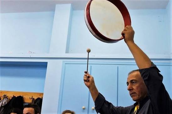 Ο παιδαγωγός Ηλίας Πίτσικας, εμψυχωτής θεατρικού παιχνιδιού της ομάδας «Πάροδος», δίνει τον ρυθμό με ένα τύμπανο πλαισίου σε εργαστήριο για γονείς στο 6ο Δημοτικό Σχολείο Πύργου (Σεπτέμβριος 2017). Με τον ήχο και τη χειρονομία ο εμψυχωτής συντονίζει την κίνηση και την προσοχή της ομάδας. Η δράση πραγματοποιήθηκε στο πλαίσιο της συμμετοχής του σχολείου στο 20ό Διεθνές Φεστιβάλ Κινηματογράφου Ολυμπίας για Παιδιά και Νέους.