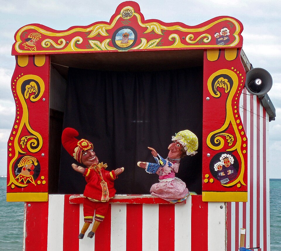 Παραδοσιακό θεατράκι Punch and Judy [Παντς και Τζούντυ] στο Swanage [Σουόνατζ] του Dorset [Ντόρσετ] της Αγγλίας. Το βρετανικό αυτό είδος κουκλοθεάτρου, με ρίζες στην ιταλική κομμέντια ντελλ άρτε και τη μορφή του Pulcinella [Πουλτσινέλλα], στήνεται σε όρθια, στενή παράγκα, όπου ο/η κουκλοπαίκτης/κουκλοπαίκτρια εμψυχοποιεί τις γαντόκουκλες πάνω από το κεφάλι του/της. Φωτογραφία: ALoan, 2006. 