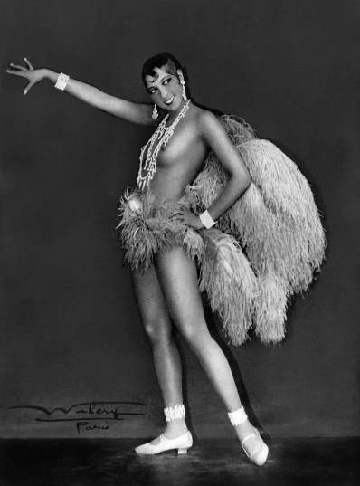 Η Josephine&nbsp;Baker (1906-1975) σε εμβληματική φωτογράφιση του στούντιο Waléry [Βαλερύ] των Παρισίων (περ. 1926), με κοστούμι από φτερά στρουθοκαμήλου, μαργαριταρένια κοσμήματα και λευκές γόβες, σε χορευτική στάση θριάμβου. Η Αφροαμερικανή ερμηνεύτρια, εμβληματική φιγούρα της Jazz Age, καθιέρωσε το γυμνό (ή ημίγυμνο) σκηνικό σώμα ως κεντρικό εκφραστικό μέσο της παρισινής επιθεώρησης του Μεσοπολέμου στις παραστάσεις της στα Folies Bergère [Φολί Μπερζέρ].
