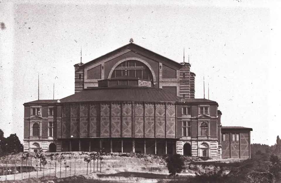 Ιστορική φωτογραφία του Bayreuther Festspielhaus [Φεστιβαλικού Θεάτρου του Μπαϋρόιτ] πριν από το 1882, χωρίς την προσθήκη του βασιλικού οικήματος [Königsbau]. Σχεδιασμένο από τον Richard Wagner σε συνεργασία με τον αρχιτέκτονα [[#Otto Brückwald [Όττο Μπρύκβαλντ]#]] και εγκαινιασμένο το 1876 με την πρώτη ολοκληρωμένη παράσταση του Το Δαχτυλίδι των Νιμπελούνγκεν [Der Ring des Nibelungen, 1874], το θέατρο αποτελεί την αρχιτεκτονική και θεσμική υλοποίηση της βαγκνερικής σύλληψης του ολοτεχνήματος. 