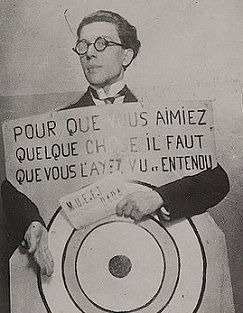 Ο [[#André Breton [Αντρέ Μπρετόν]#]] ως άνθρωπος-σάντουιτς στην ντανταϊστική βραδιά του Théâtre de l'Œuvre στο Παρίσι (27 Μαρτίου 1920). Η πινακίδα του [[#Francis Picabia [Φρανσίς Πικαμπιά]#]] απευθυνόταν ευθέως στο κοινό: «Για να αγαπήσετε κάτι πρέπει να το έχετε δει και ακούσει εδώ και πολύ καιρό, συνωμοταξία ηλιθίων». Η πρόκληση των θεατών ήταν δομικό στοιχείο της ντανταϊστικής δράσης.