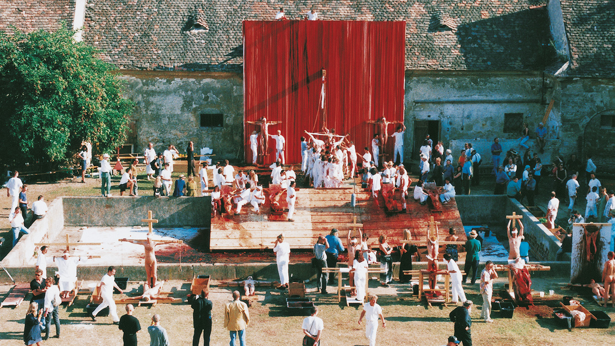 Hermann Nitsch, Das Orgien Mysterien Theaters [Θέατρο των Οργίων και των Μυστηρίων], 3- 9 Αυγούστου 1998, Πρίντσεντορφ. Σταδιακά ο Nitsch εγκατέλειψε την ζωγραφική (στην οποία θα επέστρεφε αργότερα) και αφιερώθηκε ήδη από το 1958 στην δημιουργία συλλογικών παγανιστικο-χριστιανικών τελετουργιών, οι οποίες εκλαμβάνονταν ως ολοτεχνήματα [Gesamtkunstwerk] και καλούσαν το κοινό και τους συμμετέχοντες/τις συμμετέχουσες να τις προσλάβουν με όλες τους τις αισθήσεις. Τα έργα αυτά, ο Nitsch τα ονόμασε Das Orgien Mysterien Theaters  [Θέατρο των Οργίων και των Μυστηρίων] και αποσκοπούσαν να αναπαραστήσουν σε διάρκεια έξι (6) ημερών ένα κράμα αρχαίας τραγωδίας, Σαίξπηρ, Φάουστ κ.ά. υπό το πρίσμα των Freud και Jung. Το αποτέλεσμα ήταν μια άμεση αισθητηριακή εμπειρία, κατά την οποία οι θεατές/θεάτριες δοκίμαζαν, μύριζαν, έβλεπαν, άκουγαν, άγγιζαν κ.ά. Το Θέατρο των Οργίων και των Μυστηρίων επαναλήφθηκε συχνά, με διαφορετική διάρκεια κάθε φορά.  Όλες οι προηγούμενες δράσεις θεωρήθηκαν από τον καλλιτέχνη προπαρασκευαστικές της εξαήμερης δράσης που πραγματοποιήθηκε το καλοκαίρι του 1998 στον ιδιωτικό τού Πύργο στην Αυστρία. Οι δράσεις αυτές, οι οποίες συνεχίστηκαν και μετά το 1998, αποσκοπούσαν στην συλλογική κάθαρση μέσω της τελετουργικής βίας και θυσίας, όπου αναδύεται μια αρχέγονη και εκστατική εξύμνηση της ζωής.  