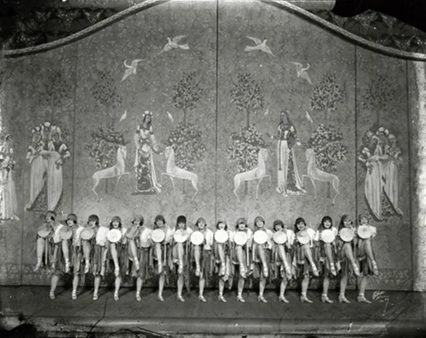 Χορευτικό νούμερο των Ziegfeld Follies [Ζήγκφελντ Φόλλις] του Florenz Ziegfeld [Φλόρενς Ζήγκφελντ], Νέα Υόρκη, δεκαετία του 1920. Η ευθύγραμμη διάταξη του γυναικείου χορού μπροστά σε ζωγραφιστό φόντο τεκμηριώνει τα θεαματικά μπαλέτα και τους ζωντανούς πίνακες που καθιέρωσε η επιθεώρηση, πρακτικές που πέρασαν στο αμερικανικό μιούζικαλ ως αυτοτελή νούμερα συνόλου.
